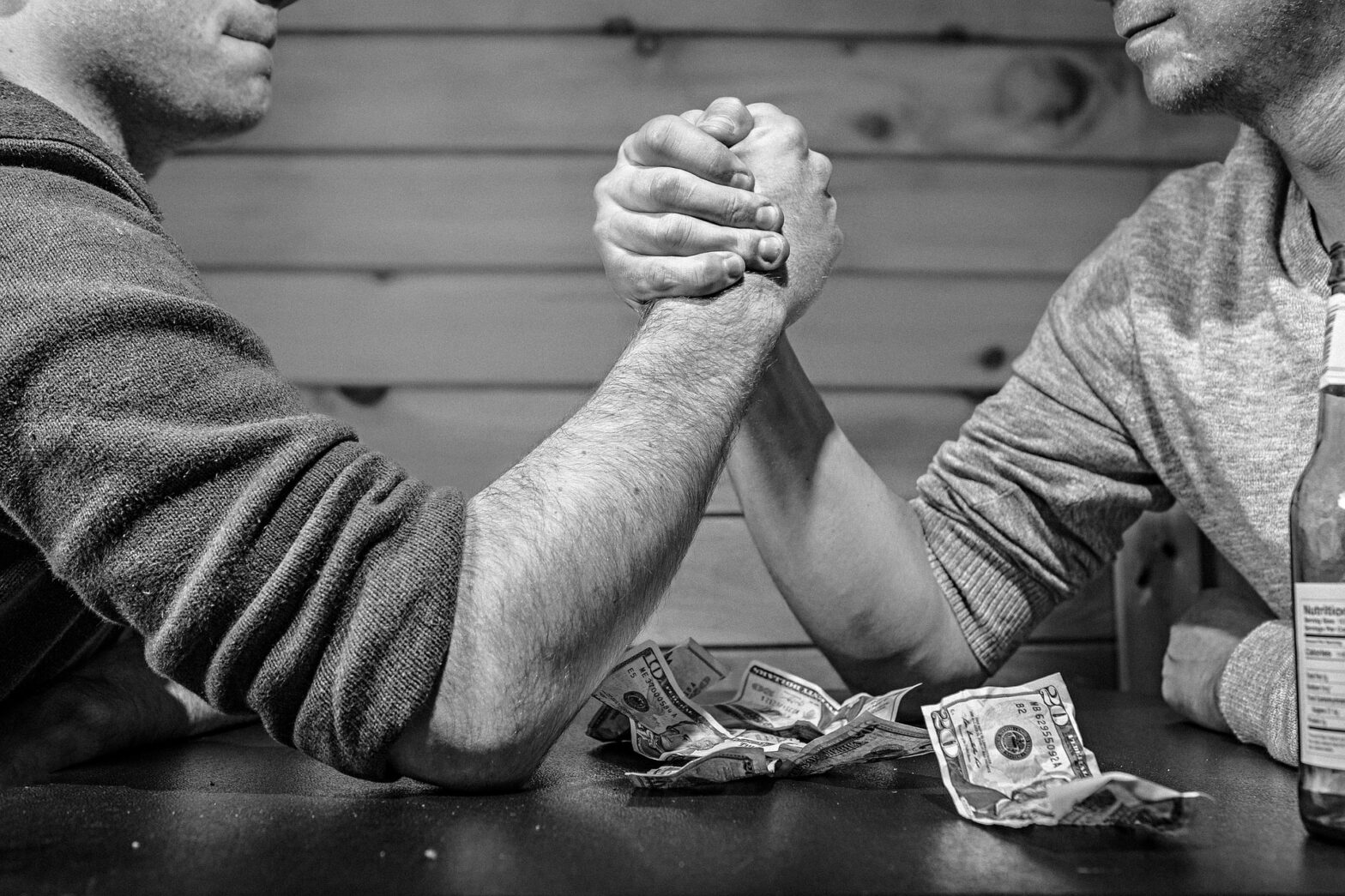 Two men arm wrestle for money.